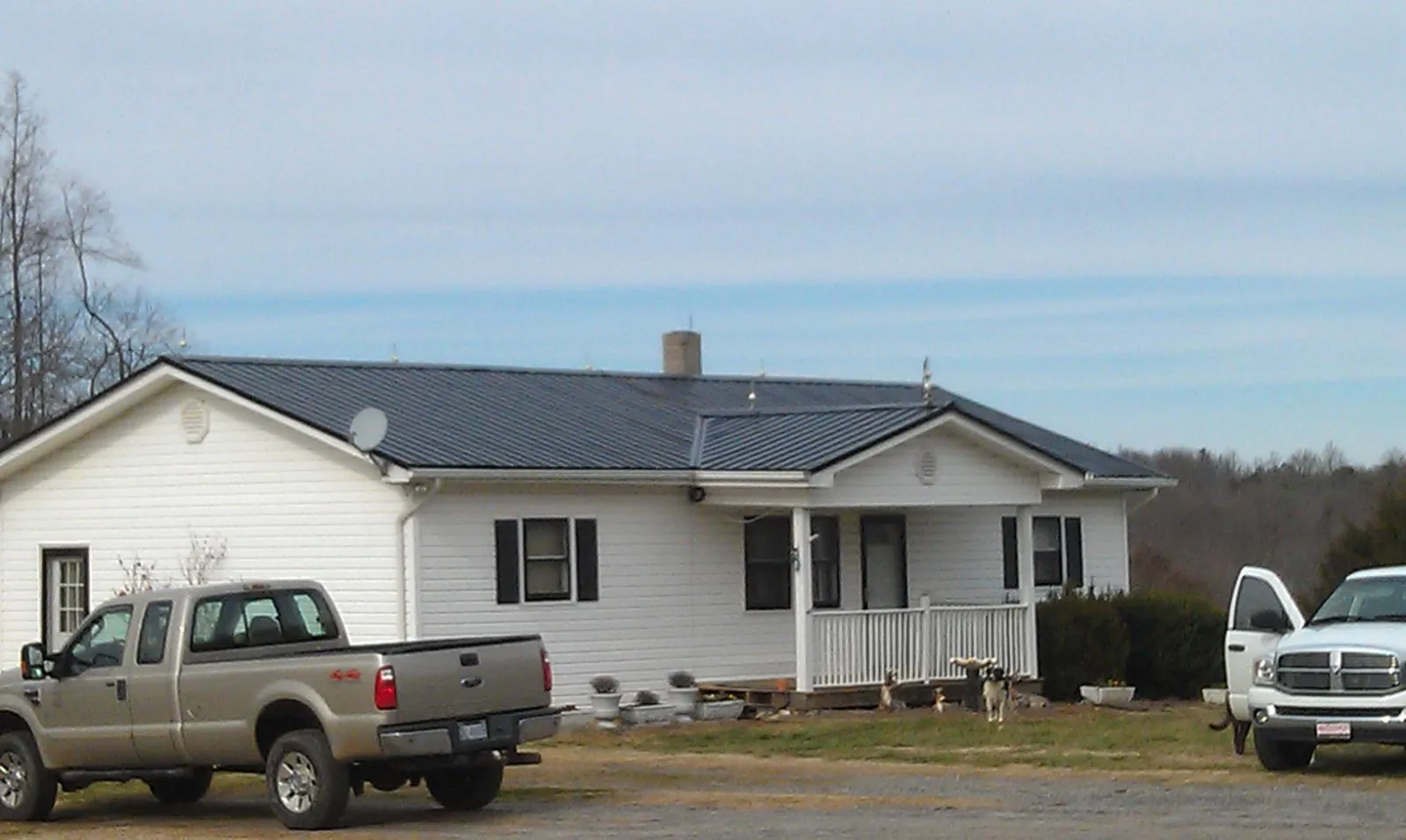 Finished dark metal roof on a white ranch home with work trucks parked in Dover